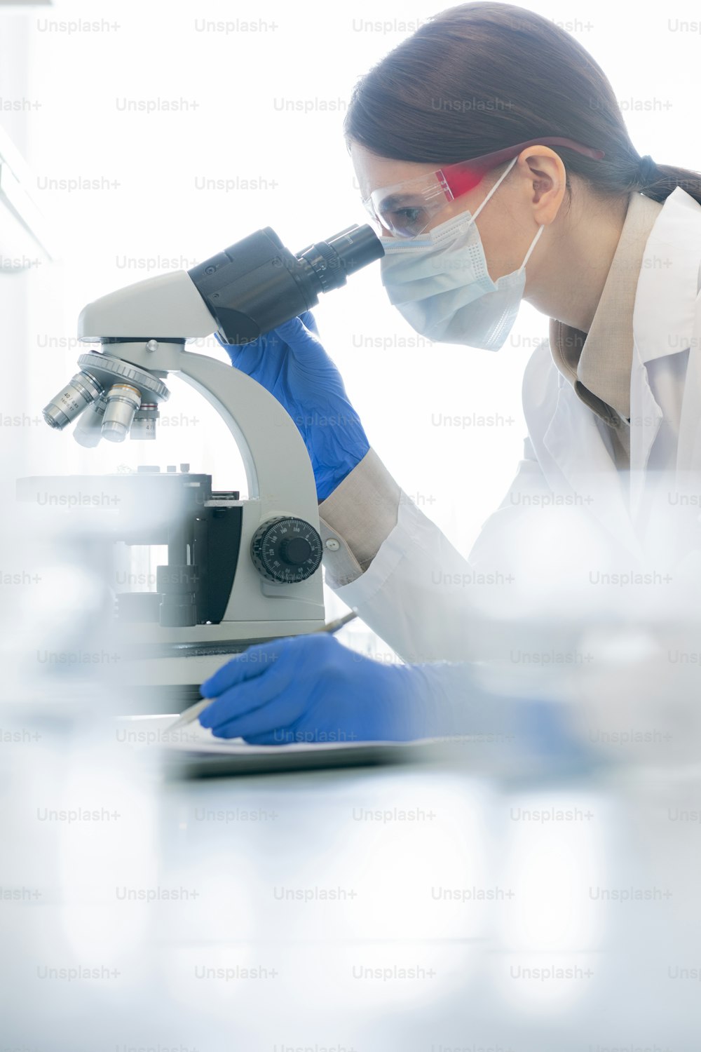 Vertical side view shot of unrecognizable female medical scientist examining specimen chemical reaction using microscope in modern laboratory
