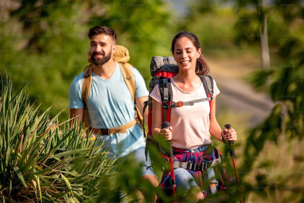 Hikers with backpacks and hiking sticks walking through forest together.