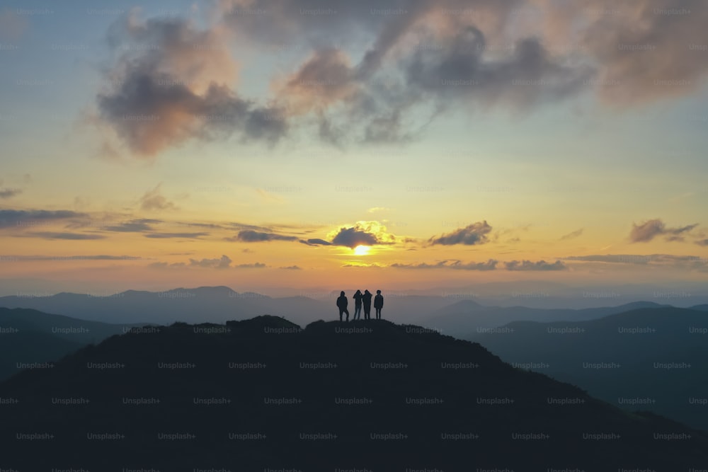 Las cuatro personas de pie en la hermosa montaña en el fondo de la puesta de sol