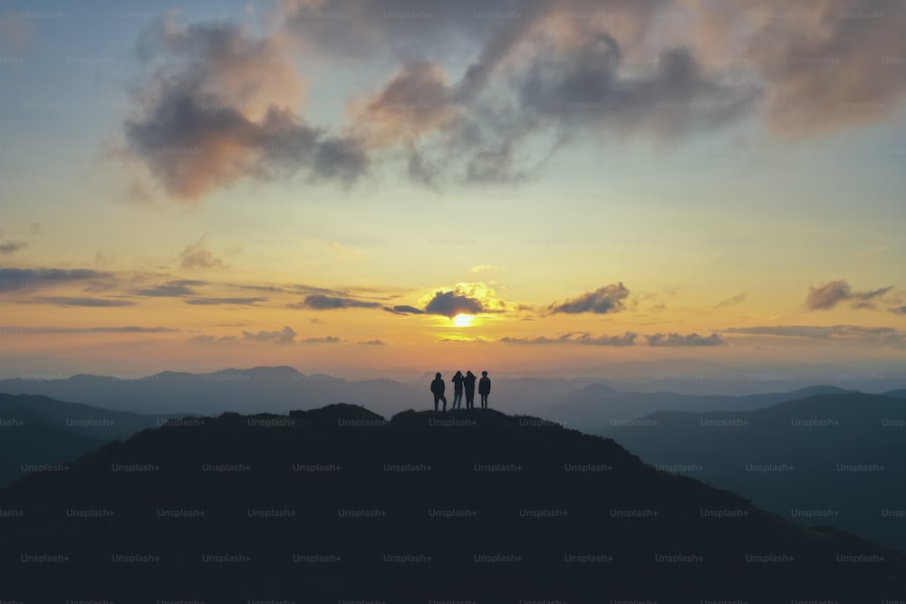 The four people standing on the beautiful mountain on the sunset background