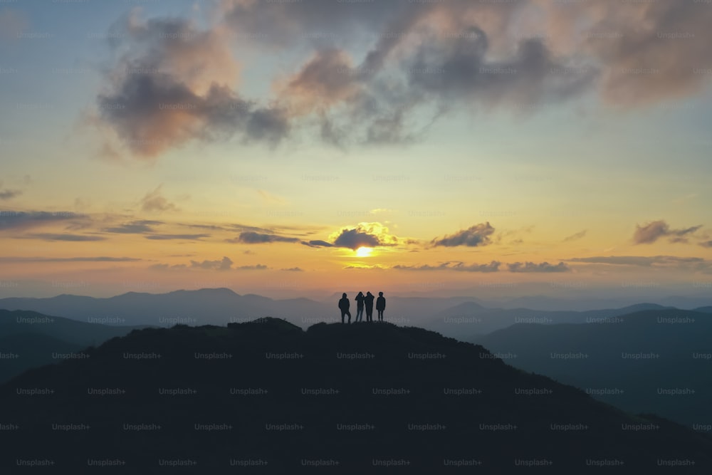 The four people standing on the beautiful mountain on the sunset background
