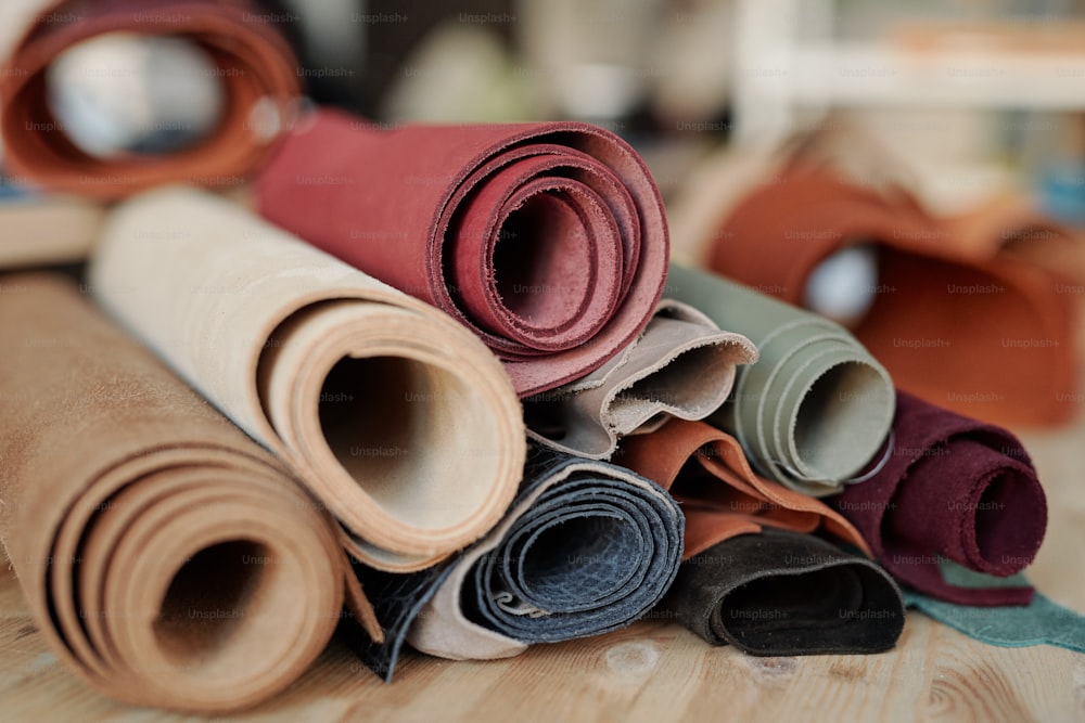 Collection de daim roulé et de cuir de différentes couleurs couché sur une table en bois à l’intérieur de l’atelier du maroquinier