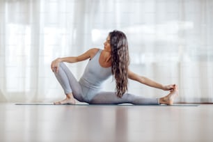 Young attractive flexible yogi girl in side lunge yoga pose. Yoga studio interior.
