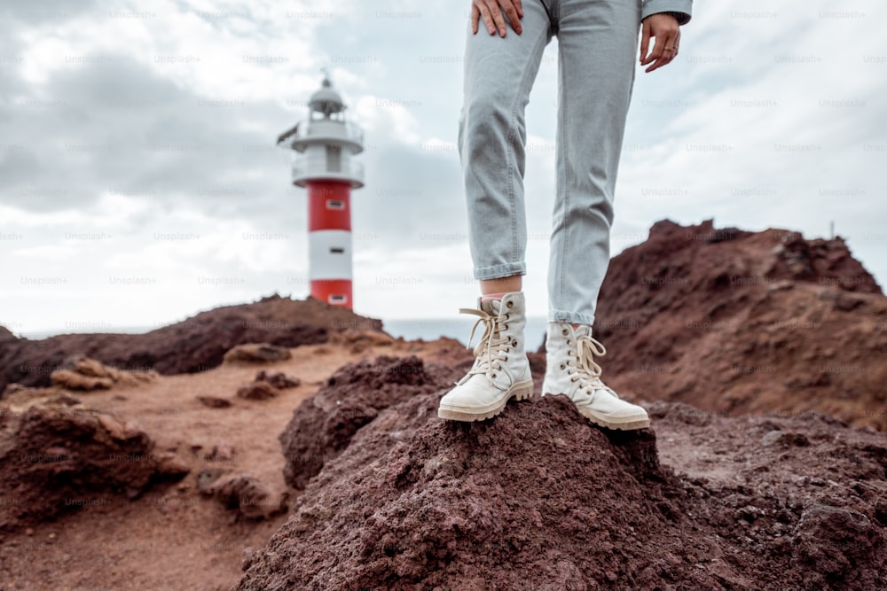Traveler standing on the rocky land, traveling volcanic landsacpes near the lighthouse. View on the woman's trekking shoes