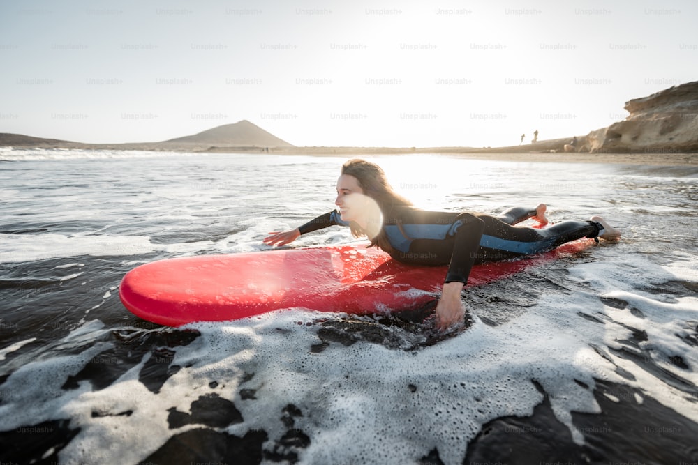 Young woman in wetsuit catching water flow on the surfboard, surfing on the wavy ocean during a sunset. Water sports and active lifestyle concept