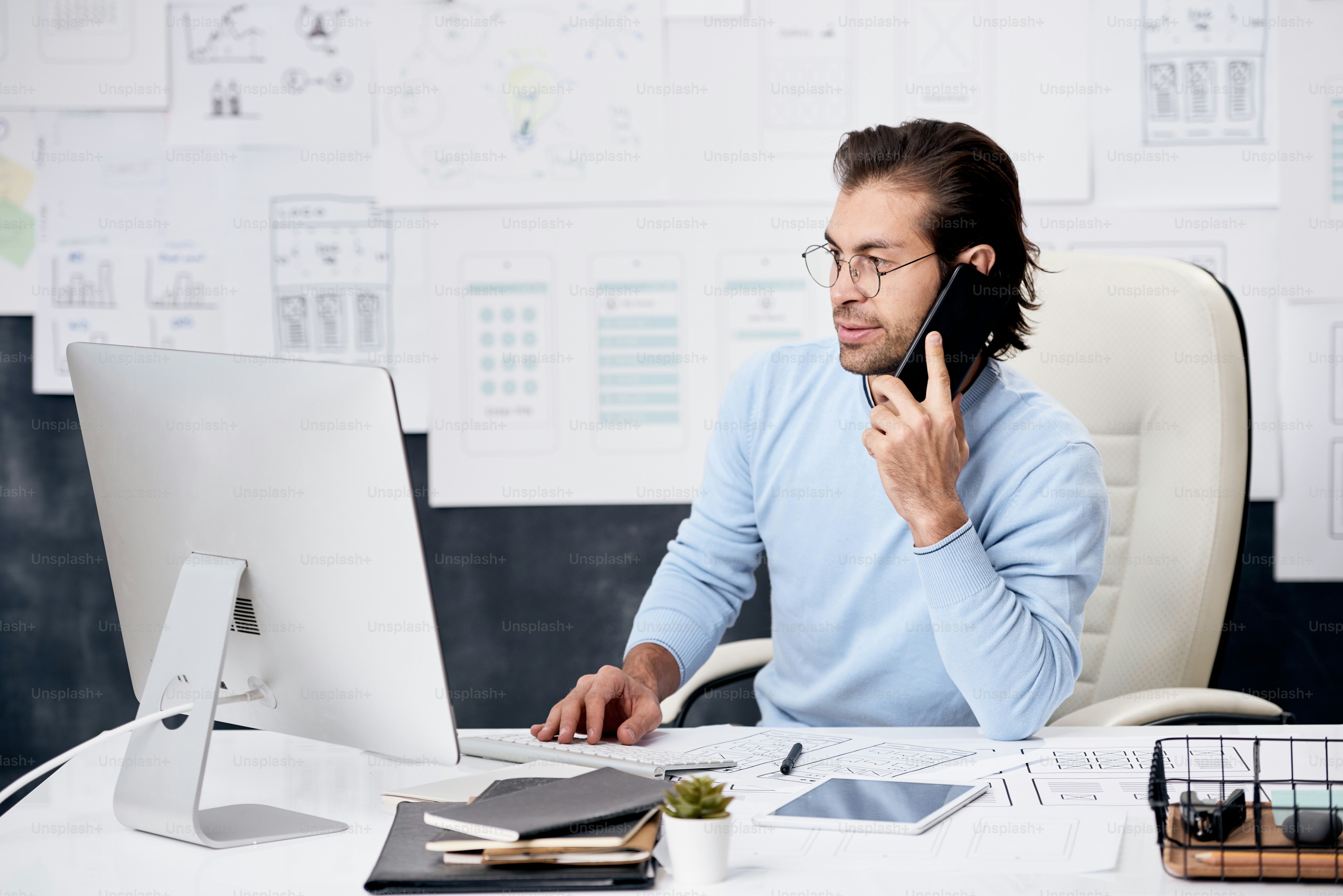 Inhalt braunhaariger Manager eines IT-Unternehmens, der am Schreibtisch sitzt und mit Kollegen per Telefon spricht, während er Daten am Computer analysiert