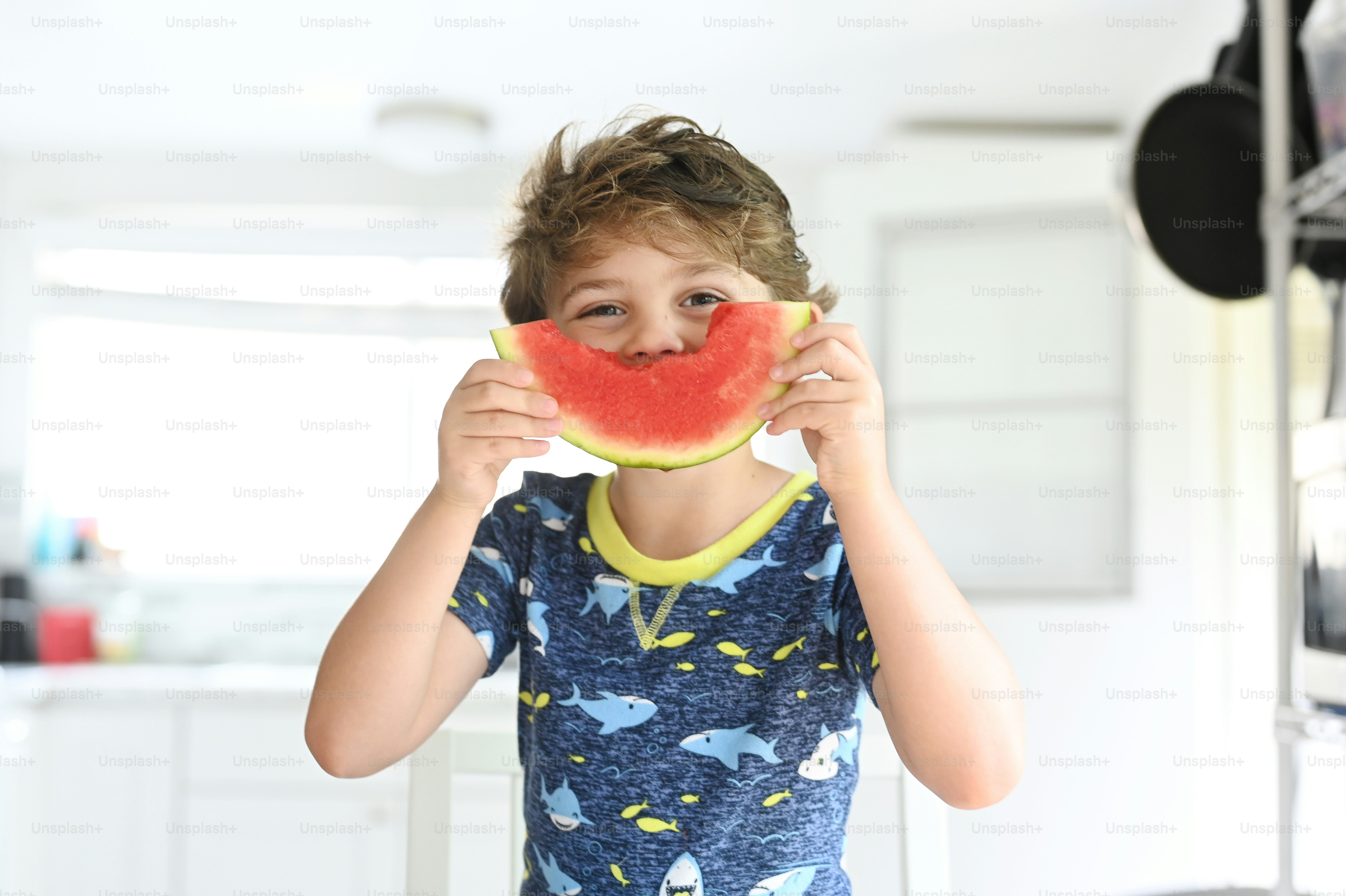 Ein kleiner Junge, der ein Stück Wassermelone vor sein Gesicht hält
