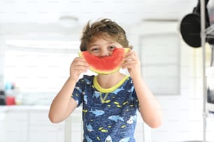 a young boy holding a piece of watermelon in front of his face