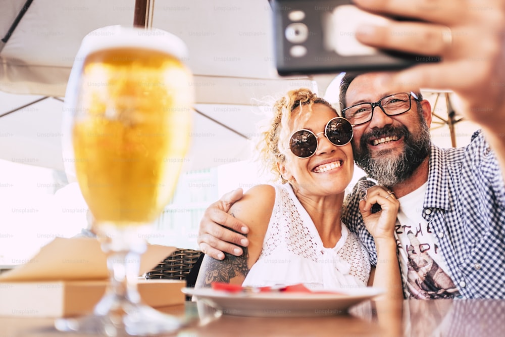 Cheerful happy people couple at the restaurant enjoying and having fun together taking selfie picture with modern phone - hug and relationship love concept for middle age woman and man