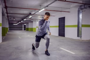 Young muscular man doing lunges in underground garage.