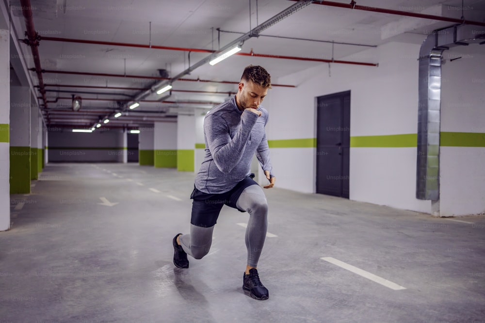Young muscular man doing lunges in underground garage.