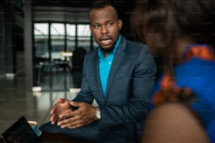 Schwarzafrikanischer Geschäftsmann diskutiert die Arbeit auf einem digitalen Tablet während eines zwanglosen Treffens bei einem Kaffee in einem Büro