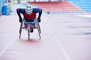 Course en fauteuil roulant. Sportif handicapé portant un casque couvrant la distance dans un fauteuil spécialisé à trois roues sur une piste extérieure