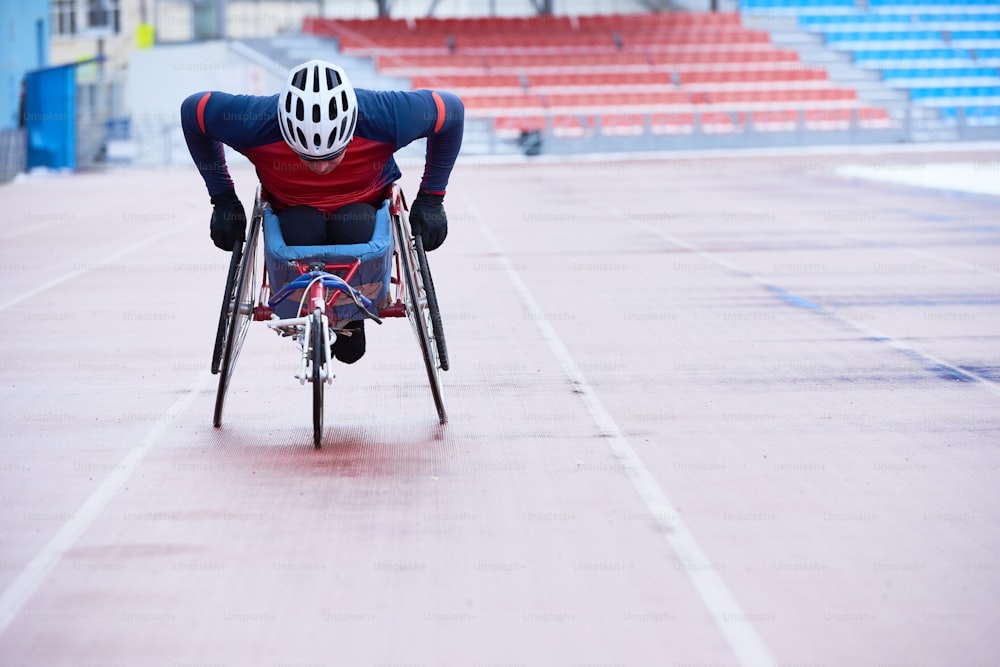 Carreras en silla de ruedas. Deportista discapacitado en casco cubriendo distancia en silla especializada de tres ruedas en pista al aire libre