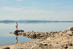 Unrecognizable young shirtless man standing on boulder and enjoying peaceful lake view on beautiful clear summer day