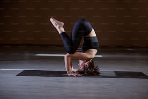Seitenansicht der flexibel fitten Yogi-Frau, die auf dem Kopf balanciert. Yoga-Studio-Interieur.