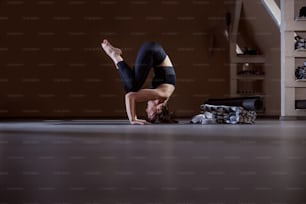 Side view of flexible fit yogi woman balancing on head. Yoga studio interior.