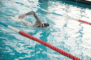 Young bearded man in cap and goggles swimming stroke in modern pool