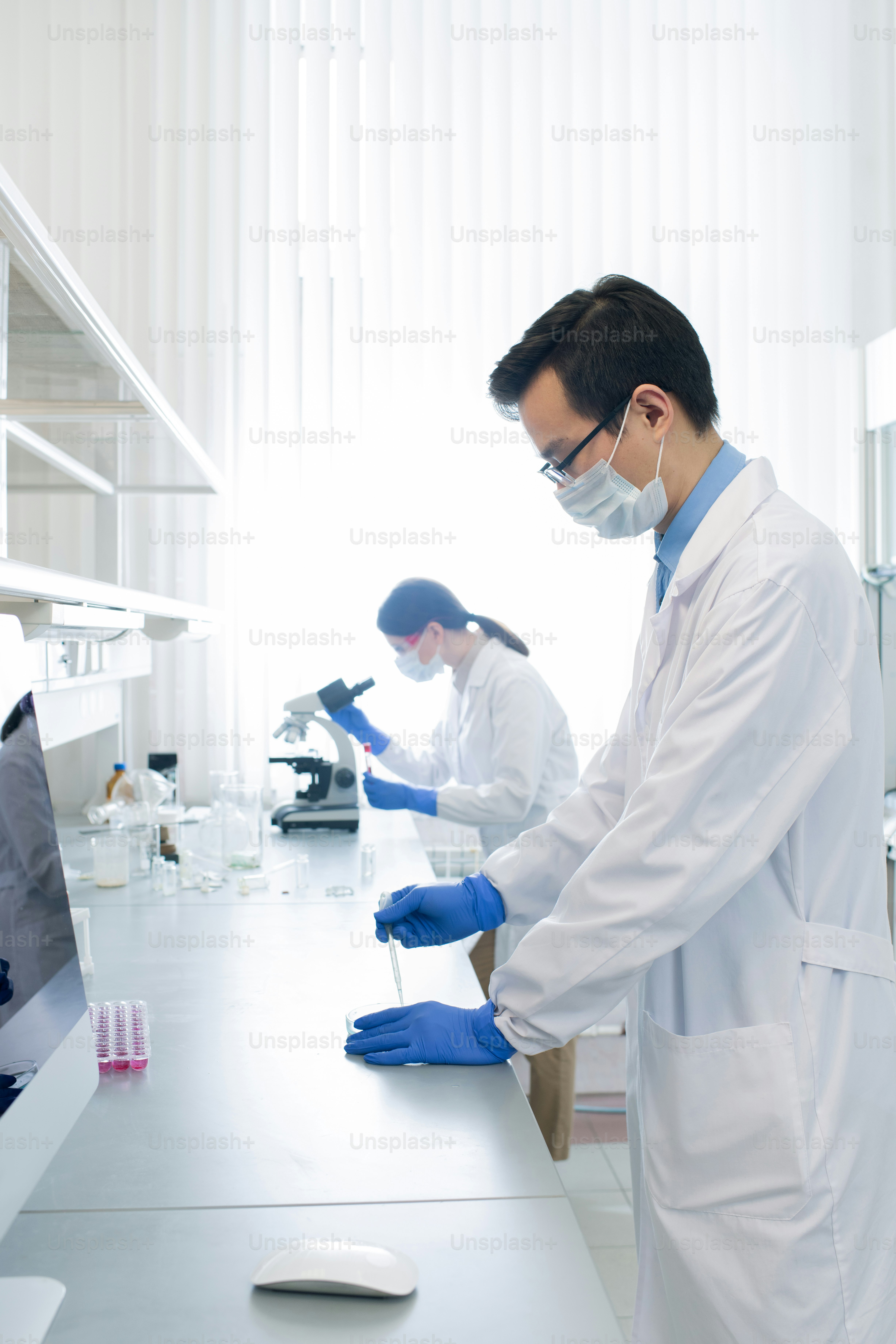 Joven farmacéutico o investigador chino que prueba una nueva vacuna mientras su colega estudia las características del virus en segundo plano