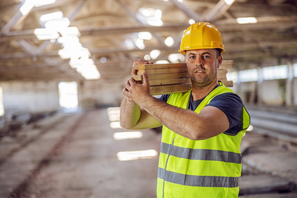 Picture of hardworking construction worker holding joists while walking on construction site.