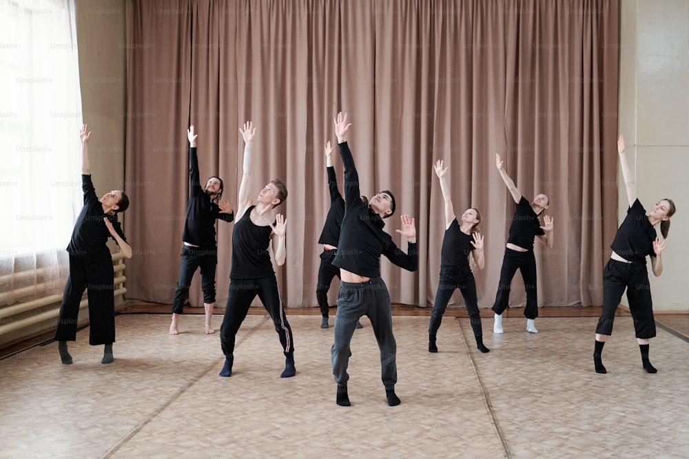 Junge Tanztrainerin zeigt Übung für eine Gruppe von mehreren Jungs und Mädchen in Aktivkleidung während des Trainings im Studio des modernen Balletts