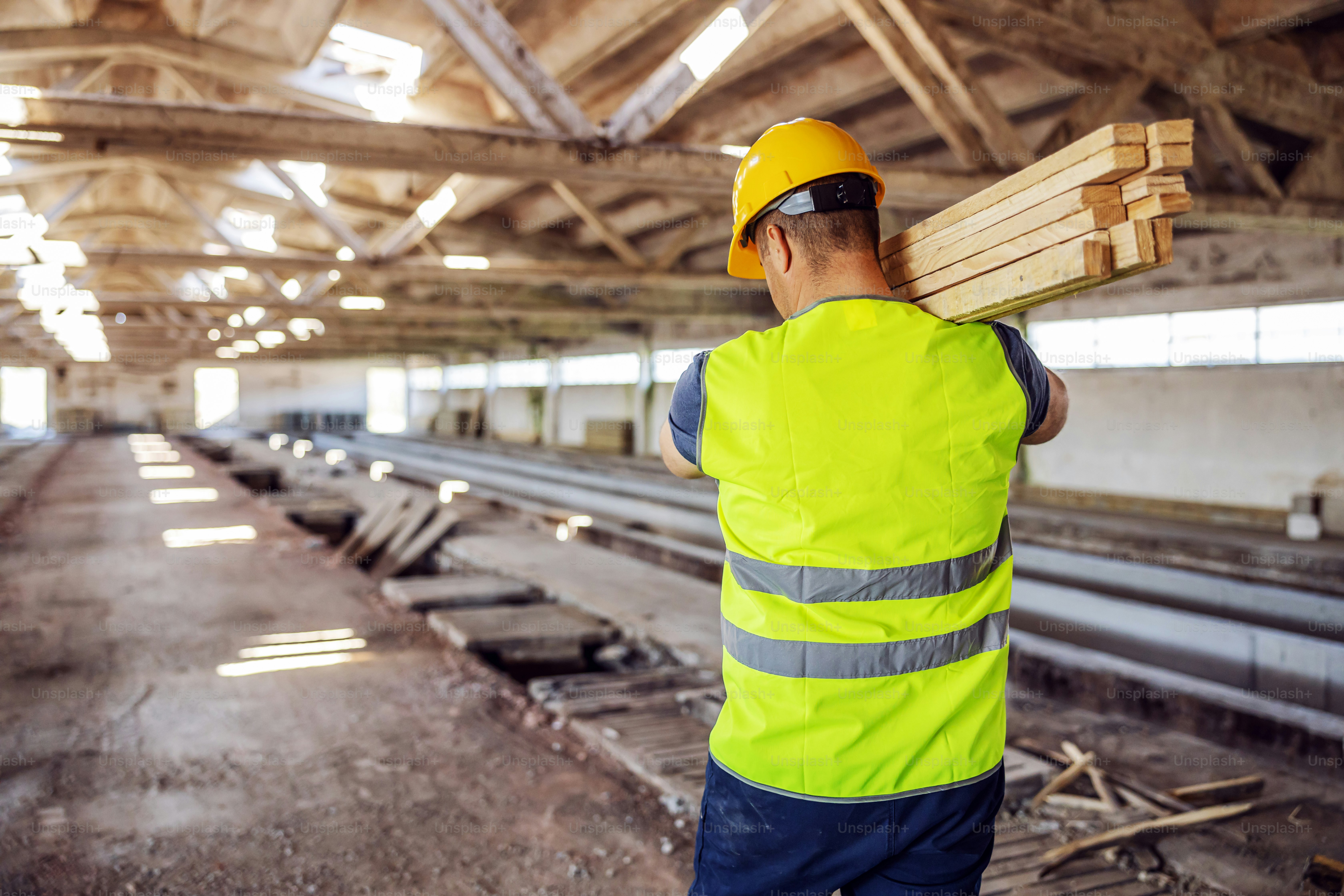 Rear view of hardworking construction worker holding joists while walking on construction site.