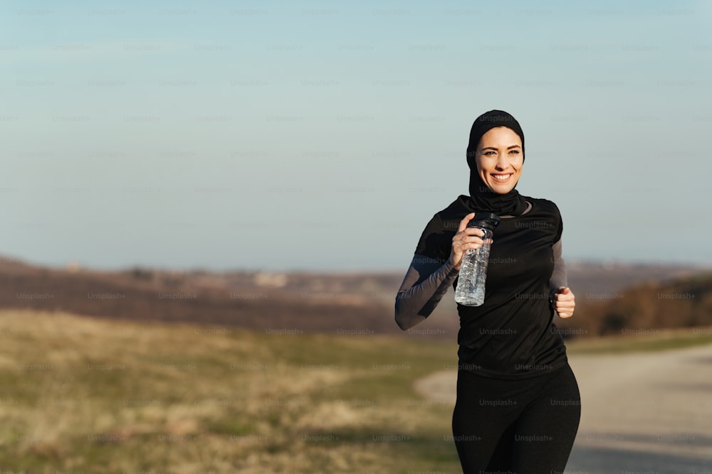 Young happy athletic woman carrying bottle of water while running in nature. Copy space.