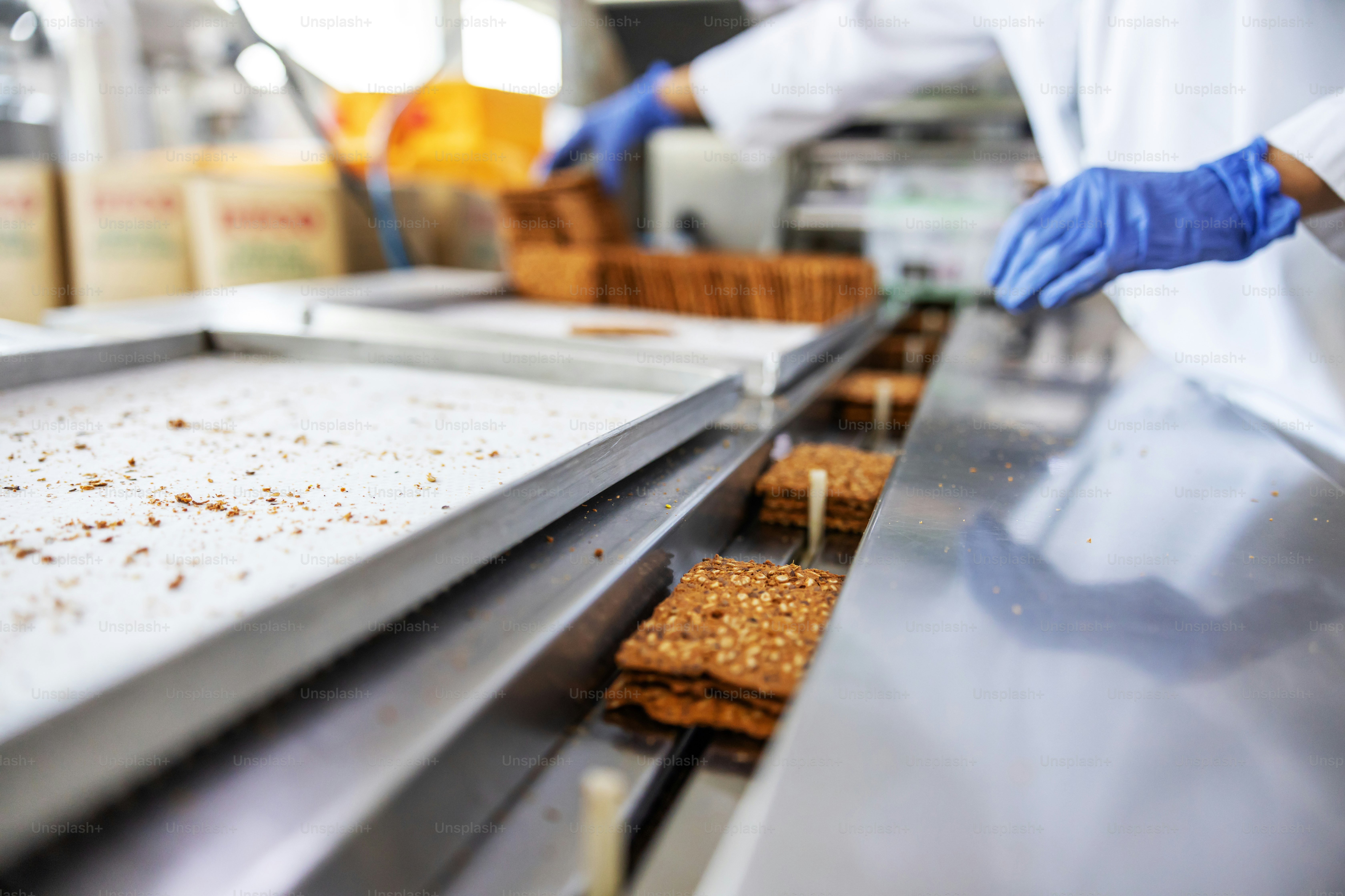 Close up do trabalhador pegando biscoitos forma máquina enquanto está em pé na fábrica de alimentos.