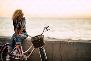 People enjoying outdoor leisure actvity looking a beautiful coloured sunset - beautiful adult young woman with long curly blonde hair  enjoy the relax after a bike tour - horizon and sun with ocean