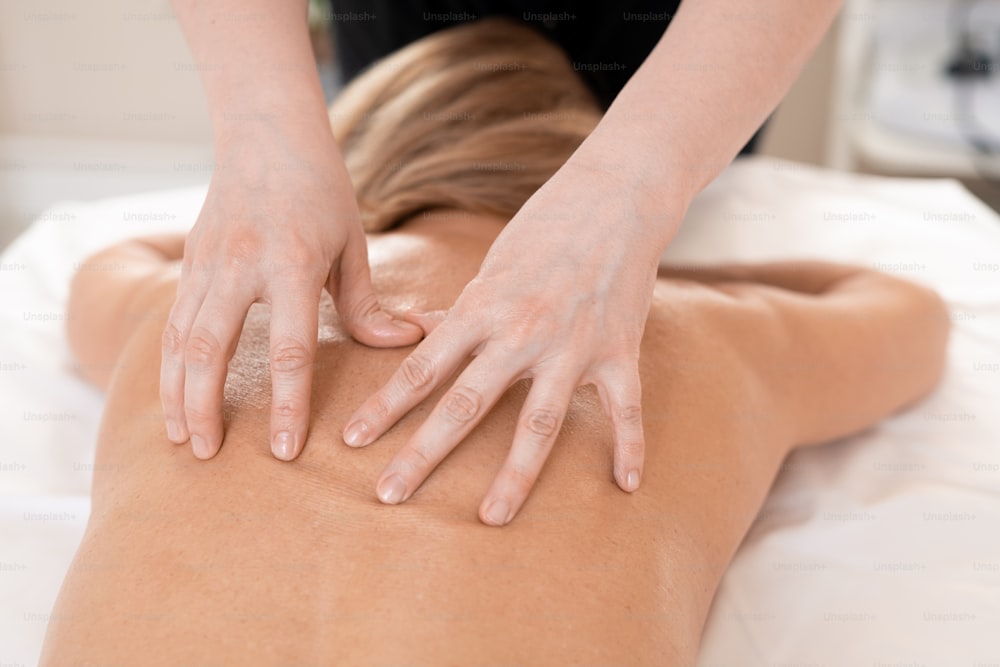 Above view of unrecognizable beauty specialist massaging naked back of woman on table in spa salon