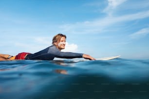 Surfeur. Homme De Surf En Combinaison Sur Planche De Surf Portrait. Mec cool nageant dans l’océan. Mer bleue et beau ciel avec des nuages doux sur le fond.