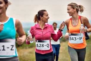 Young happy athletic women talking while running a marathon in nature.