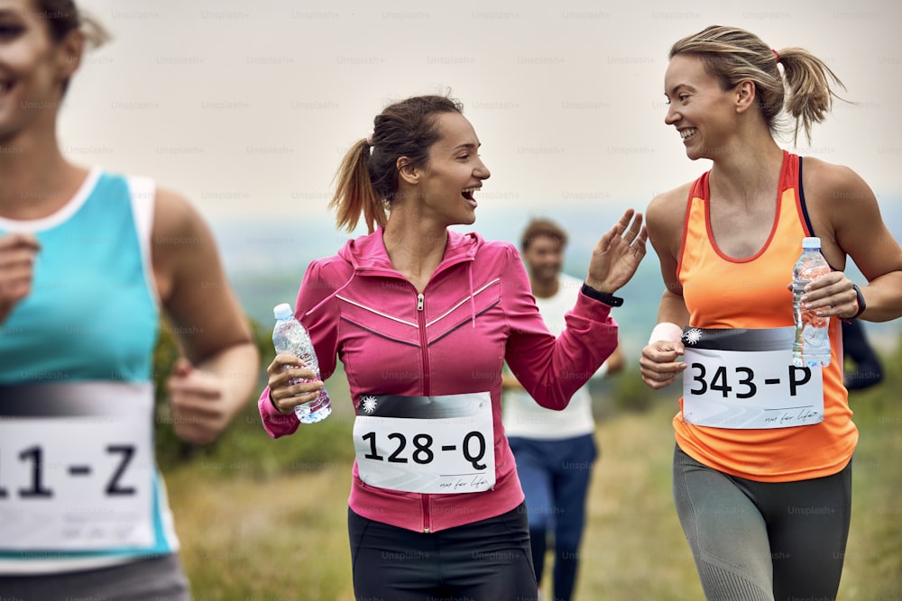 Mujeres atléticas jóvenes felices hablando mientras corren un maratón en la naturaleza.
