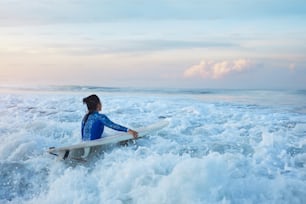 Surfing Girl. Surfer mit Surfbrett, der im Meer schwimmt. Brünette im blauen Neoprenanzug geht zum Surfen im plätschernden Meer. Wassersport für einen aktiven Lebensstil.