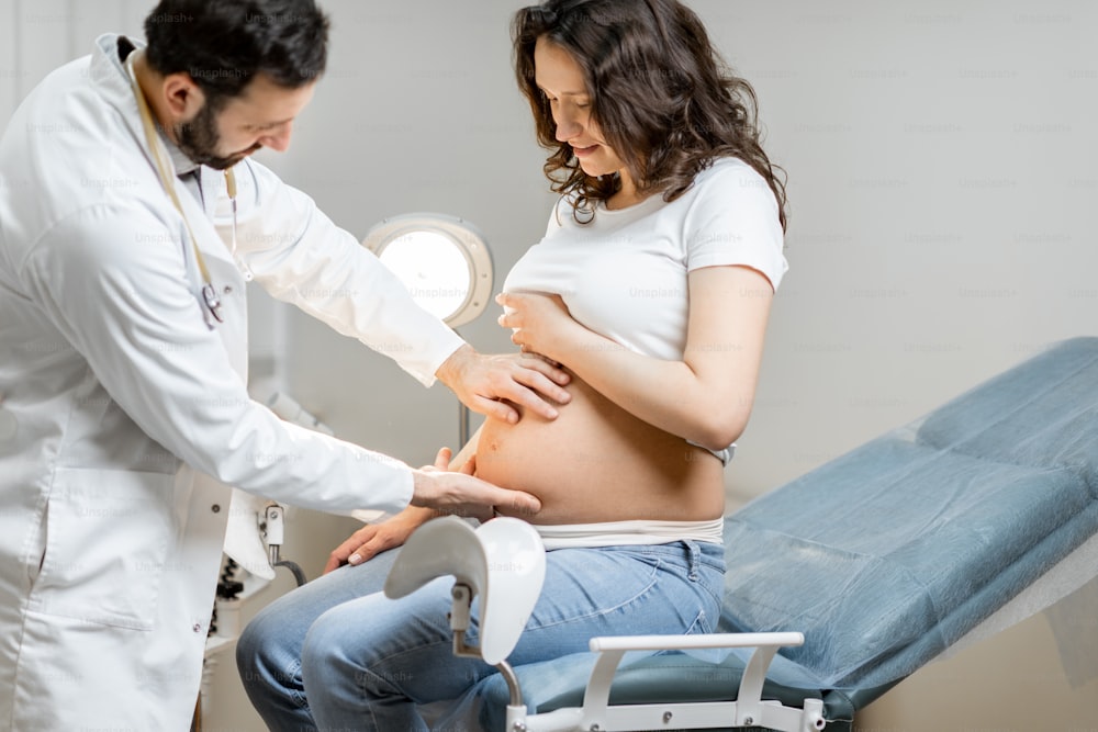 Männlicher Arzt macht eine Massage des Bauches der schwangeren Frau während einer medizinischen Untersuchung im Büro. Konzept der medizinischen Versorgung und Gesundheit während einer Schwangerschaft