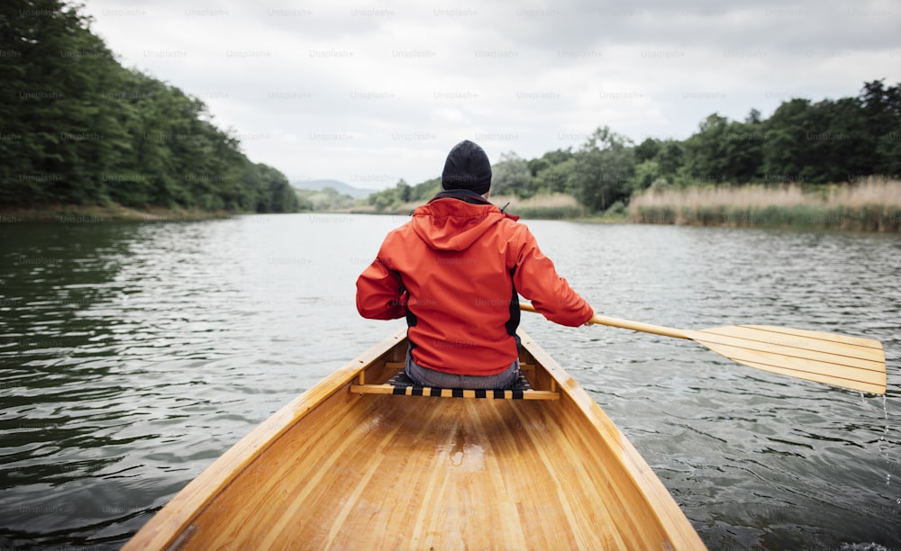 Vista trasera de un hombre remando en canoa en el lago. Paseo en barco para días lluviosos.
