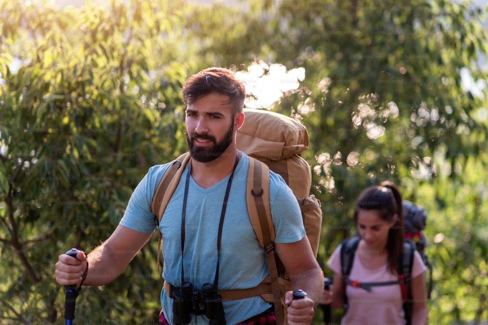 Hikers with backpacks and hiking sicks walking through forest together.