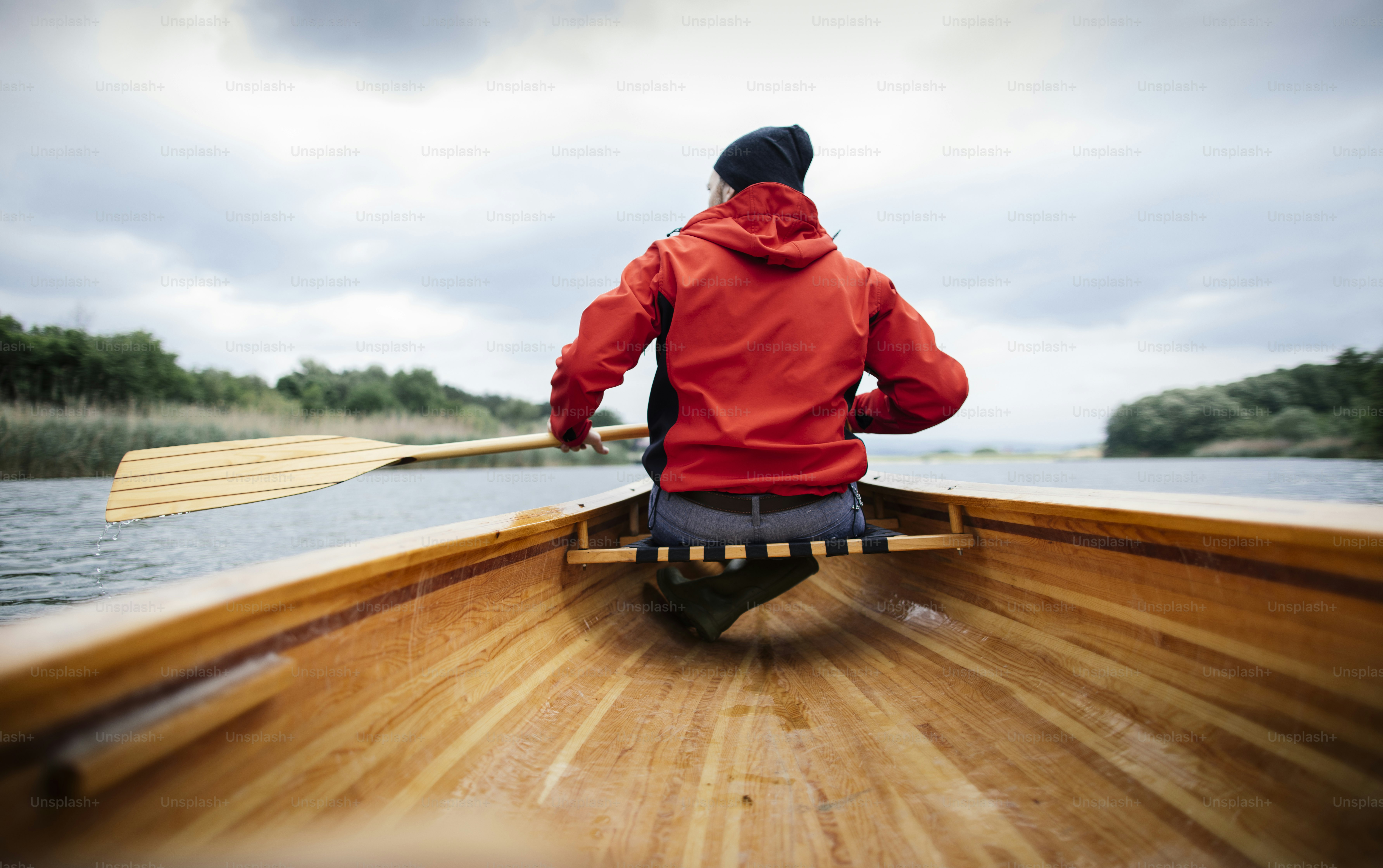 Rear view of man paddling canoe on the lake. Rainy day boat ride.
