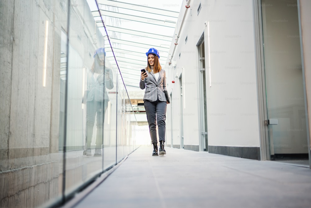 Young attractive female architect walking around building in construction process and reading an e-mail fromm important client.