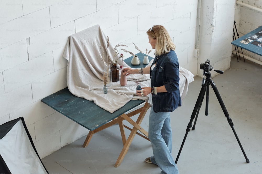 Above view of mature photographer creating composition of vases and flowers against gray fabric