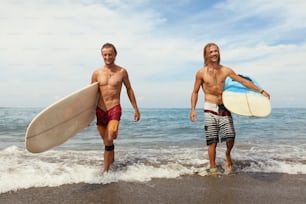 Surfing. Cheerful Young Surfers With Surfboards. Handsome Men Walking On Ocean Beach. Water Sport On Beautiful Sea Background.