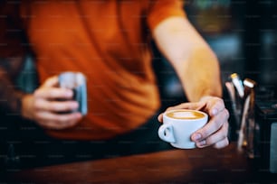 Close up of barman holding a cup of fresh morning espresso and handing it to a customer.