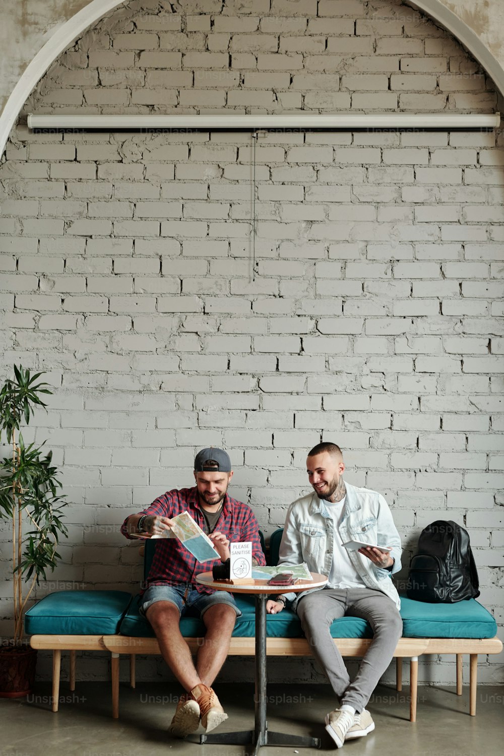 Jeunes hommes joyeux assis à table dans un café moderne au design loft et discutant de l’itinéraire du voyage tout en planifiant des vacances ensemble