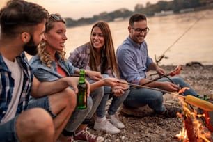 Group of people grilling sausages for dinner. Vacation, friends and lifestyle concept.