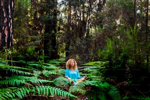 Beautiful adult lady do mindfulness exercises and yoga m editation sit down in the silence of the green nature forest - people enjoying alternative lifestyle and wood in tropical place