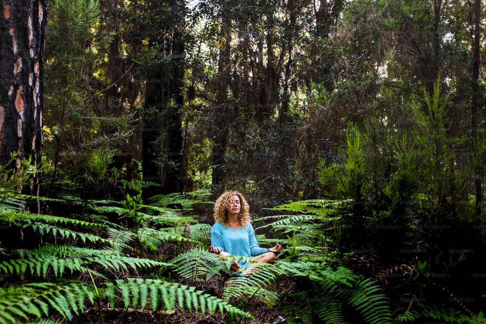 Beautiful adult lady do mindfulness exercises and yoga m editation sit down in the silence of the green nature forest - people enjoying alternative lifestyle and wood in tropical place