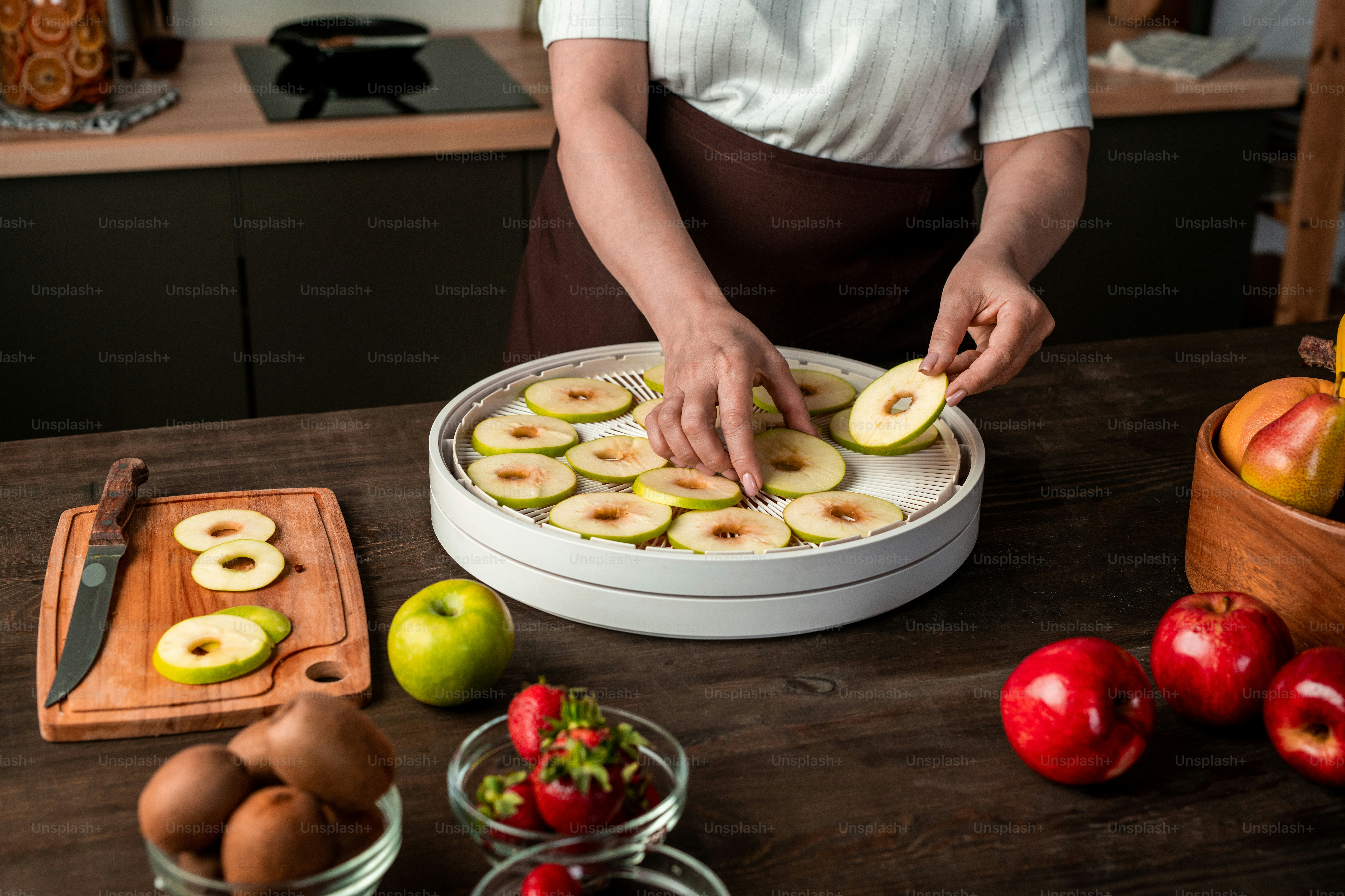 Mãos de dona de casa contemporânea colocando fatias de maçãs frescas em uma das bandejas de secadora de frutas enquanto fazia provisões para o inverno