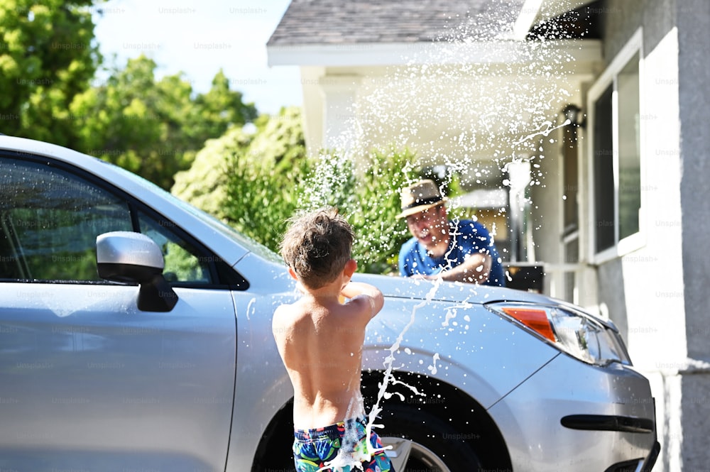 a young boy splashes water on his father's car