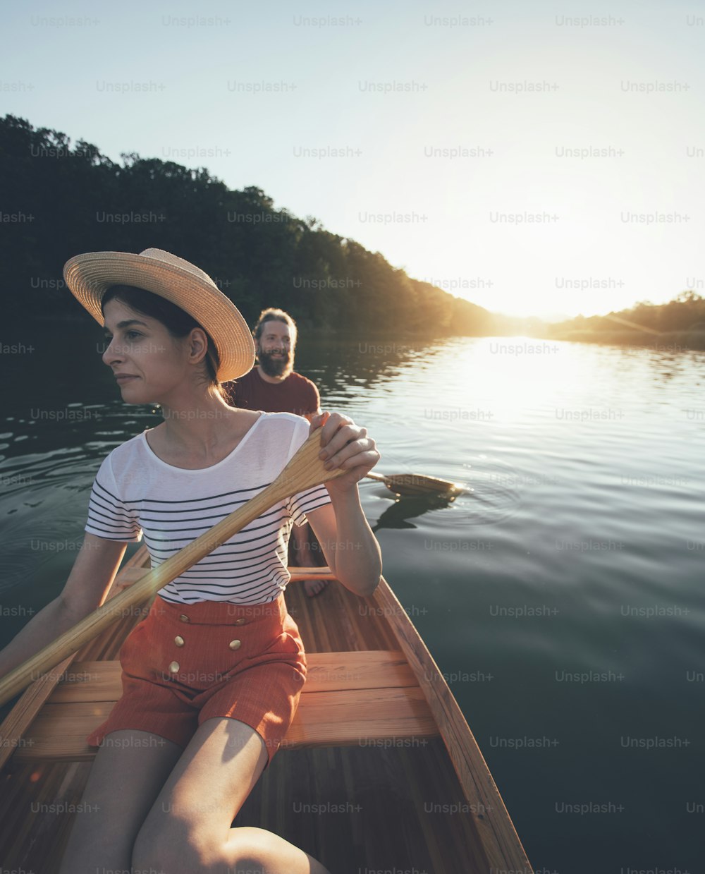 Paare paddeln Kanu auf dem Sonnenuntergangssee. Frau und Mann auf einer gemütlichen Bootsfahrt.