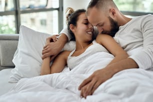 Young couple in love lying embraced on a bed. Man is kissing his girlfriend on the shoulder.